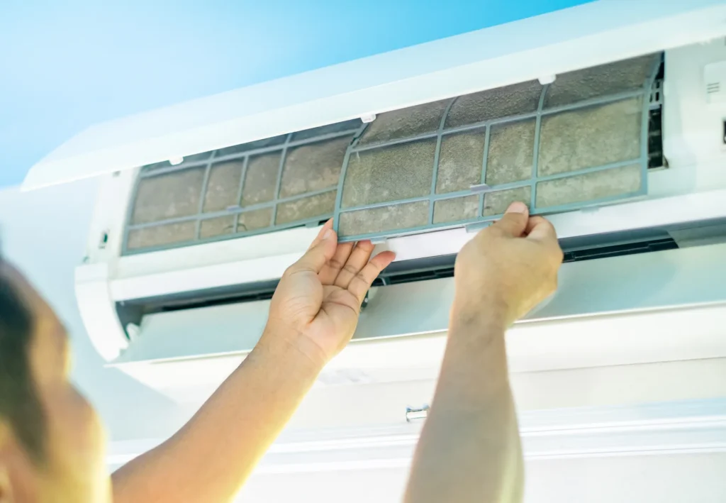 Man removing dirty air conditioner filter filled with dust for cleaning and maintenance