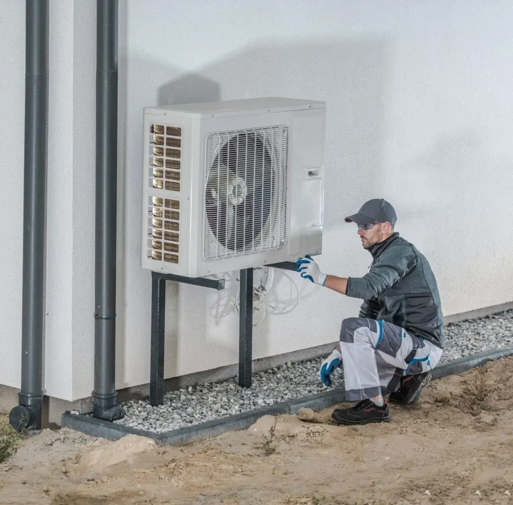 Technician inspecting a wall-mounted outdoor HVAC unit